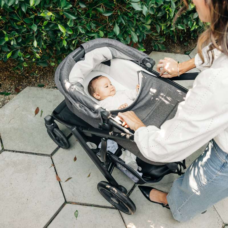 Madre colocando a su beb&eacute; en el capazo del carrito UPPAbaby Vista V2 durante un paseo al aire libre